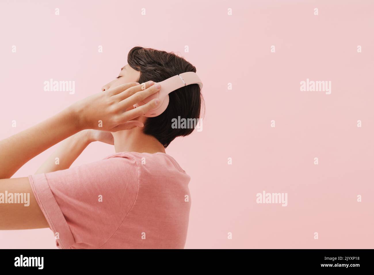 Asiatischer Junge mit T-Shirt und Kopfhörern auf rosafarbenem Hintergrund Stockfoto