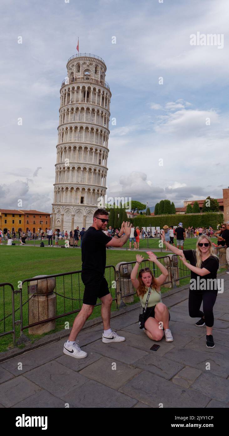 Platz der Wunder in Pisa, Toskana, Italien. Touristen posieren für Fotos vor dem Schiefen Turm von Pisa. Kathedrale links. Stockfoto