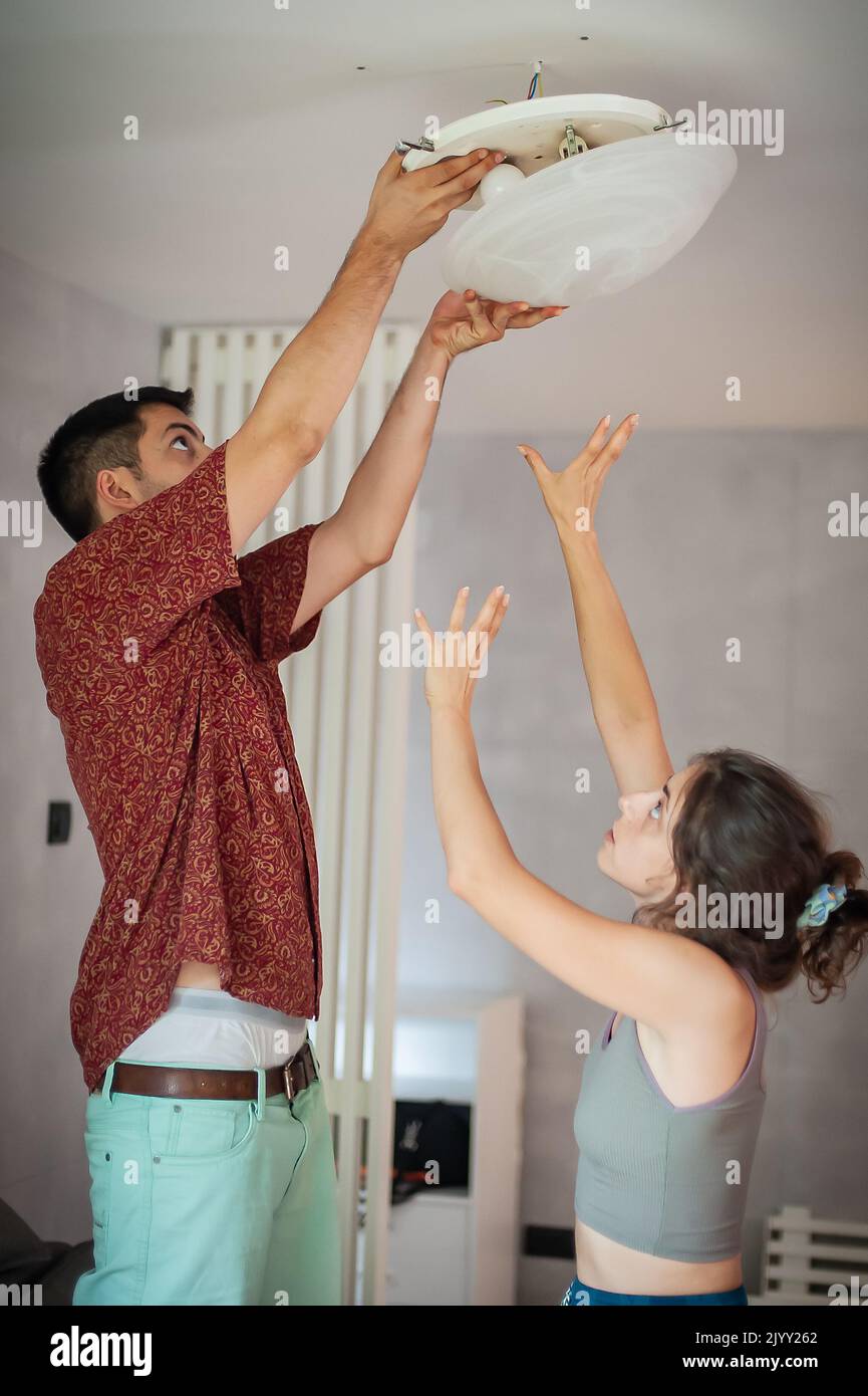 In einem gemeinsamen Leben installieren junge Männer und Frauen eine Deckenleuchte und elektrische Kabel. Do it yourself Konzept. Stockfoto