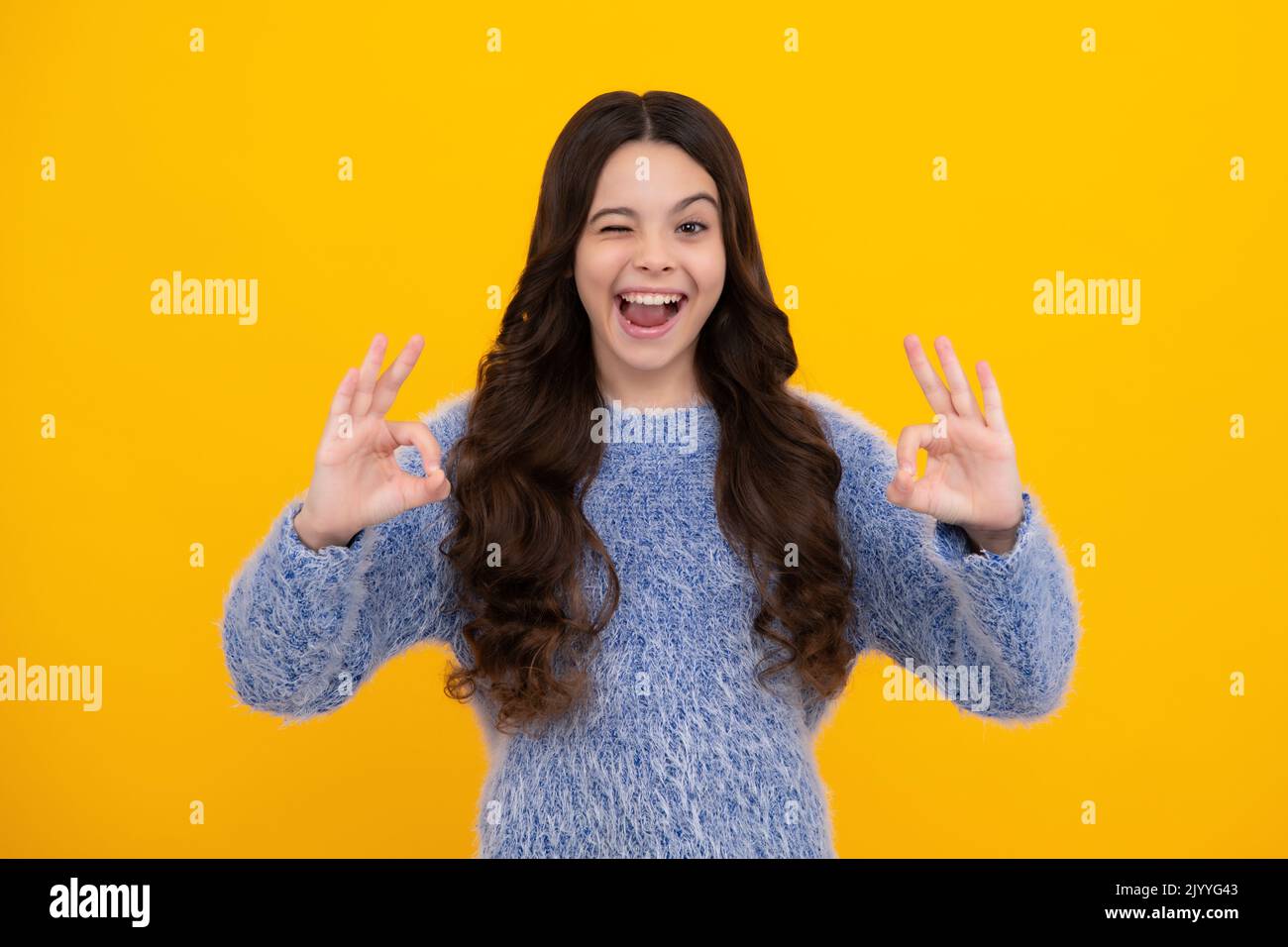 Lustige Teenager-Kind auf gelbem Hintergrund tut ok Geste und zwinkerndes mit der Hand lächelnd mit glücklichem Gesicht. Ein erstaunlicher Teenager. Aufgeregt teen Mädchen. Stockfoto