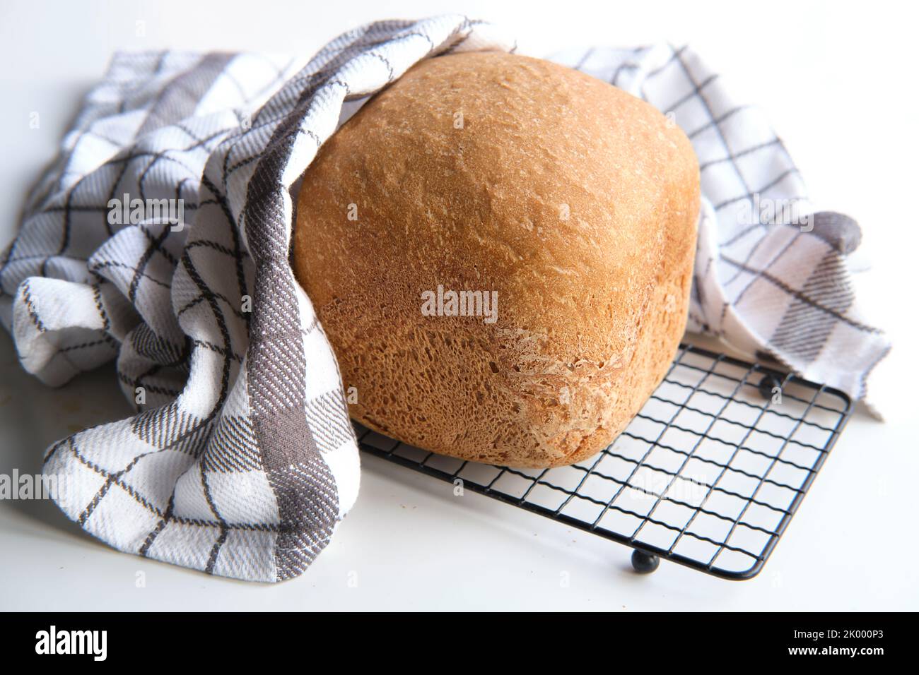 Hausgemachtes Bauernhaus gemischtes Brot. Nahaufnahme von Brot, das in der Backmaschine gebacken wurde. Vollkornbrot auf Trockengestell mit gestreifem Handtuch auf weißem Tisch Stockfoto