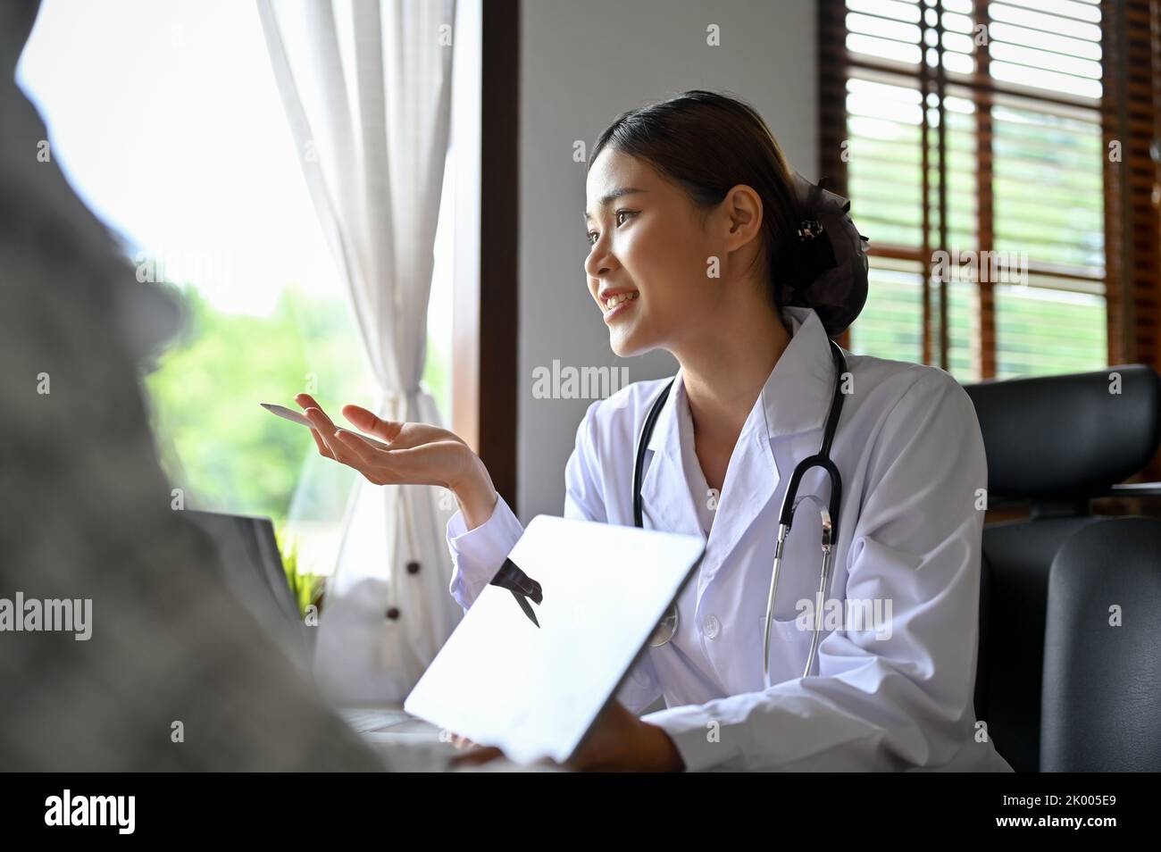 Die attraktive und kompetente asiatische Ärztin trifft sich mit ihrer Patientin im Büro und gibt ihrem Patienten medizinische und chirurgische Ratschläge. Stockfoto
