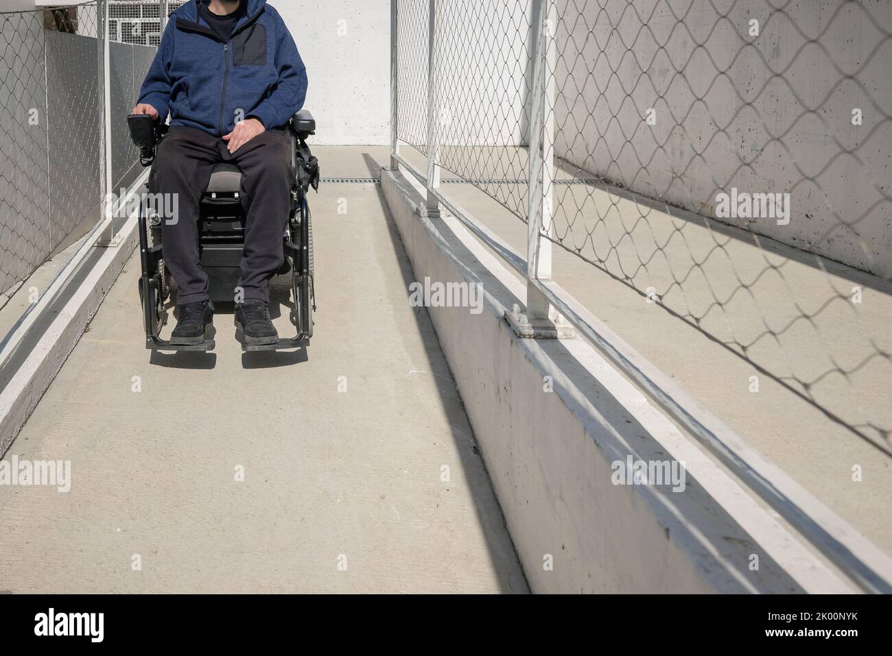 Mann auf einem elektrischen Rollstuhl, der sich entlang eines Betonwegs in der Nähe des Gebäudes bewegt. Konzept des Rollstuhlzugangs erleichtert. Stockfoto