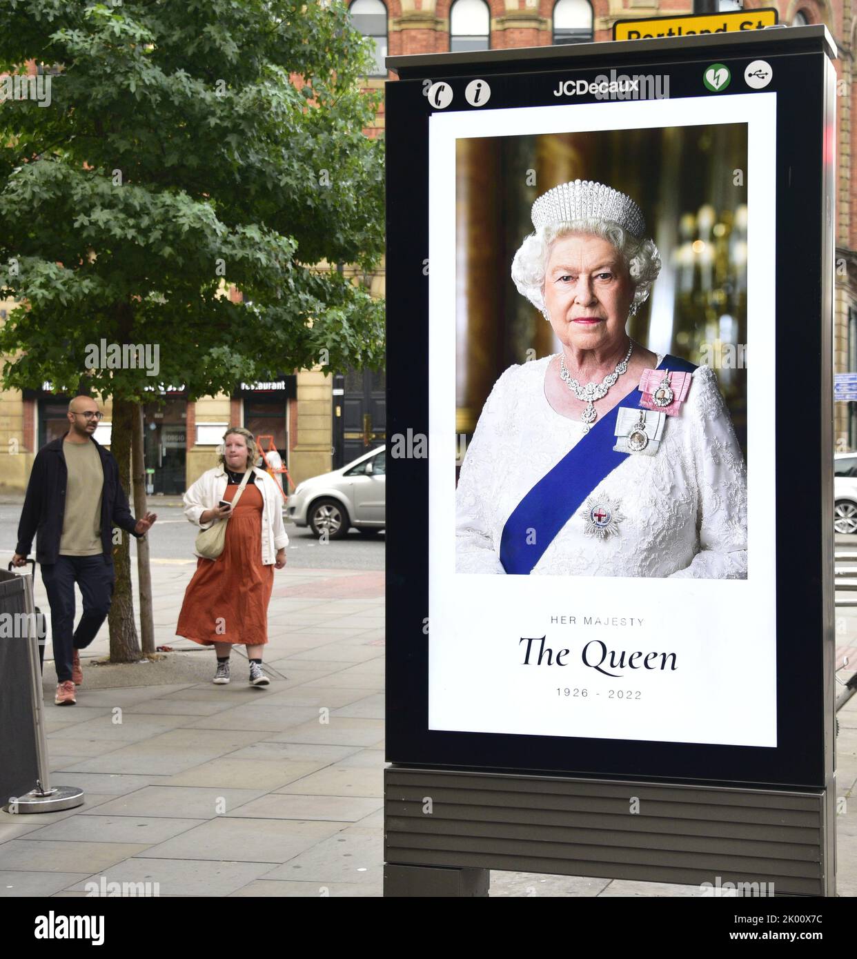 Manchester, Großbritannien, 9.. September 2022. Die Menschen gehen in Manchester, Großbritannien, an elektronischen Werbetafeln vorbei, auf denen Ihre Majestät, Königin Elizabeth II, zu sehen ist. Ihre Majestät, die Königin, starb im Alter von 96 Jahren am 8.. 2022. Der Stadtrat von Manchester hat auf seiner Website gesagt, dass die Stadt Manchester die offizielle 10-tägige Trauerperiode beobachten wird und dass: „Die Bewohner könnten Blumen zum Gedenken an den Tod Ihrer Majestät legen wollen. Am St. Ann's Square können Sie Blumen legen. Quelle: Terry Waller/Alamy Live News Stockfoto
