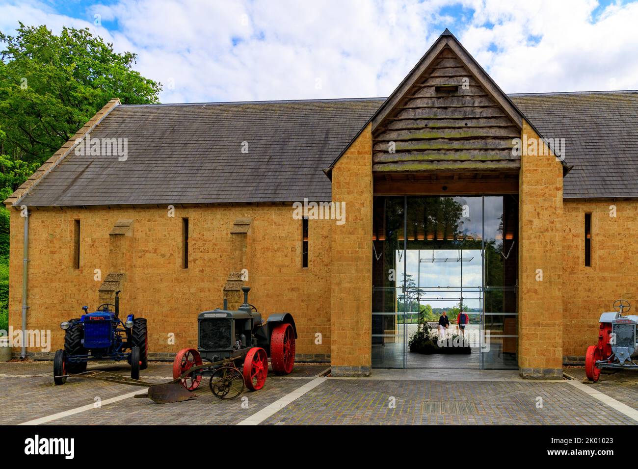 Bunte Vintage-Traktoren und Landmaschinen vor der Dreschscheune im restaurierten Garten und Hotel „The Newt in Somerset“, bei Bruton, England, Großbritannien Stockfoto