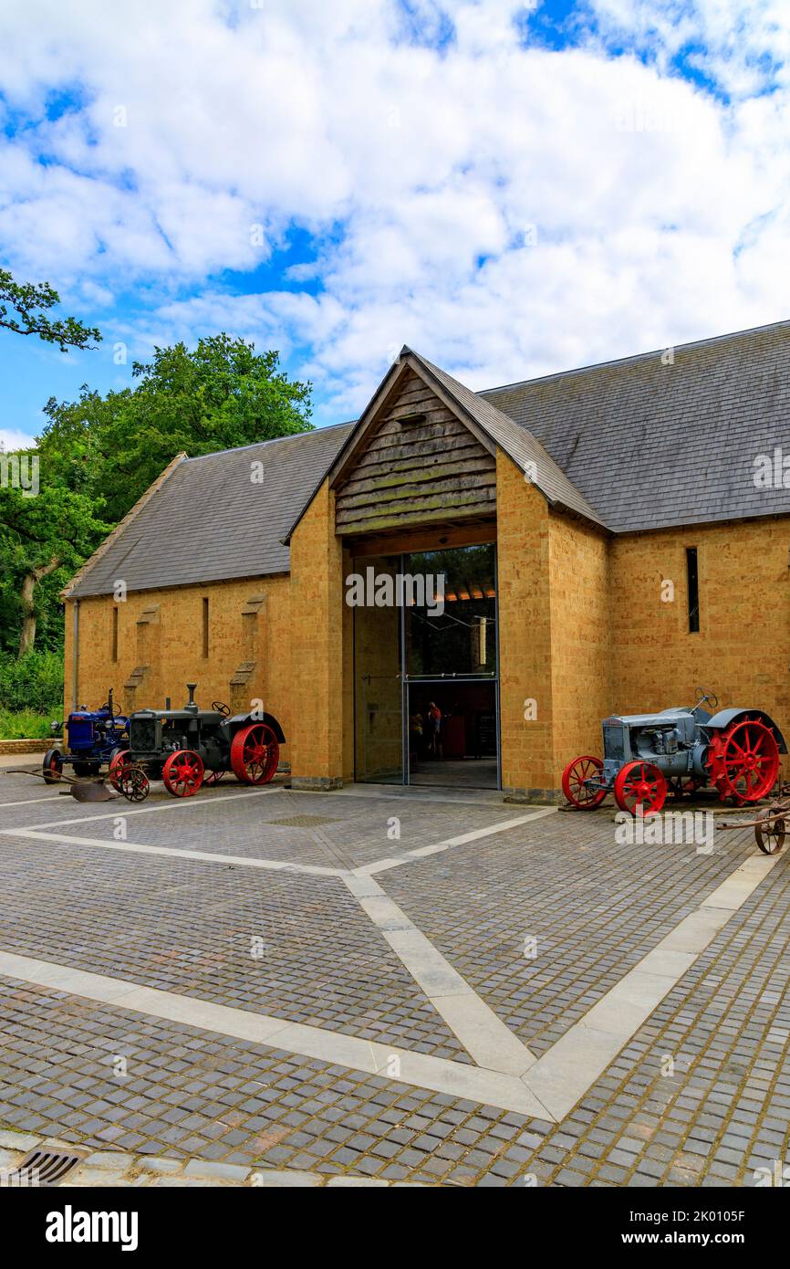 Bunte Vintage-Traktoren und Landmaschinen vor der Dreschscheune im restaurierten Garten und Hotel „The Newt in Somerset“, bei Bruton, England, Großbritannien Stockfoto