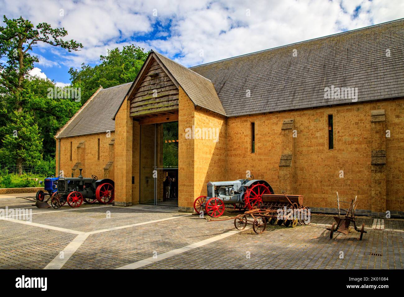 Bunte Vintage-Traktoren und Landmaschinen vor der Dreschscheune im restaurierten Garten und Hotel „The Newt in Somerset“, bei Bruton, England, Großbritannien Stockfoto