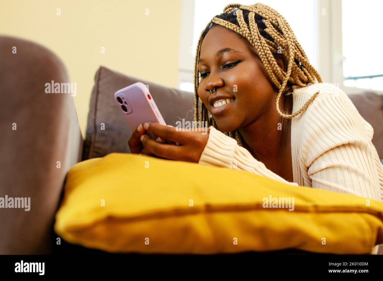 Junge afroamerikanische Frau mit Smartphone auf Couch zu Hause Stockfoto