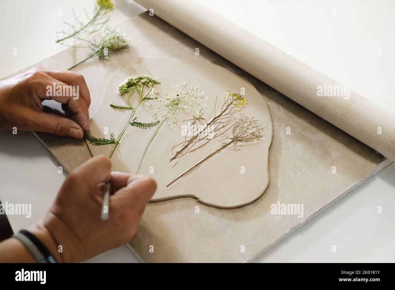 Hands Making Clay handgemachte Keramikplatten, gerollter Ton auf dem Tisch mit Pflanzen und Blumen. Draufsicht auf handgefertigte Keramik, Nahaufnahme Stockfoto
