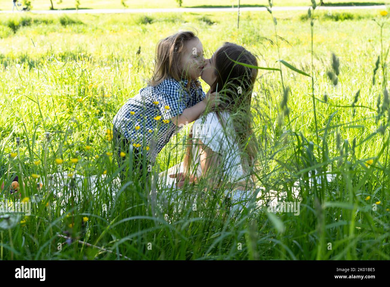 Bruder und Schwester spielen und küssen im Park inmitten des grünen Grases. Kinder umarmen sich fest. Picknick außerhalb der Stadt. Kindheit. Beziehungen. Stockfoto