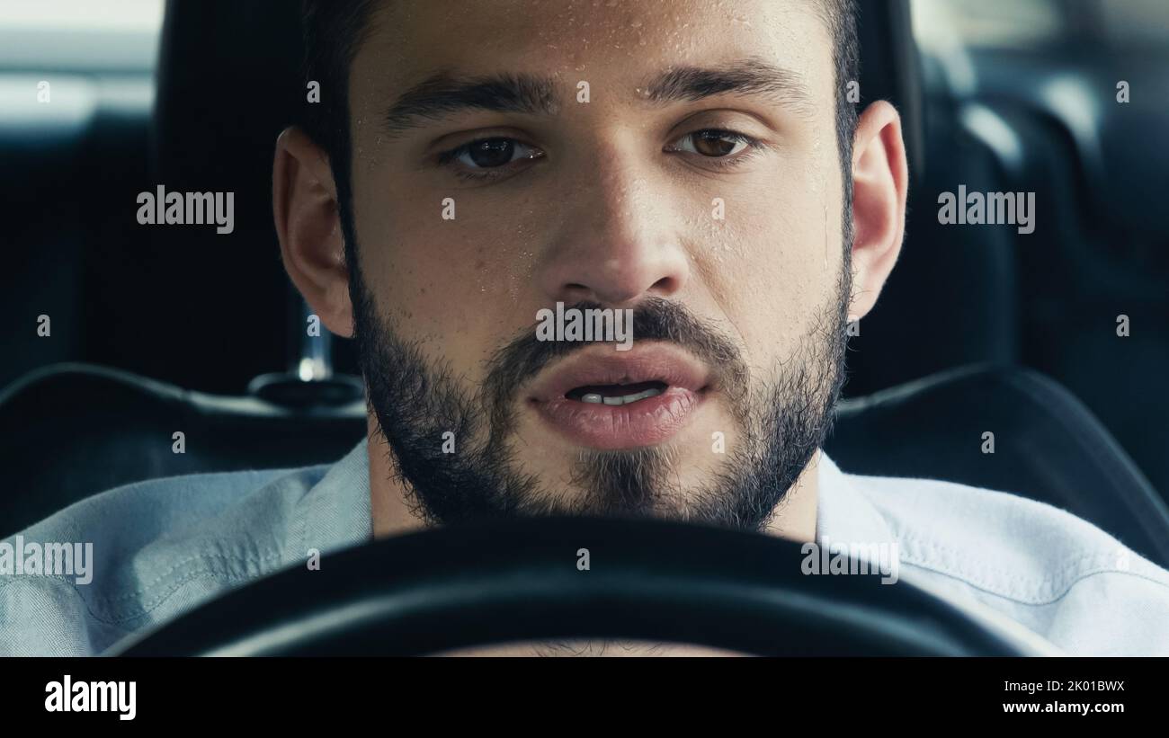 Junger bärtiger Mann mit verschwitzter Stirn, der bei heißem Wetter Auto fährt, Stockbild Stockfoto