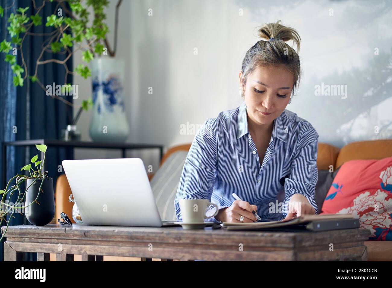 Reife professionelle asiatische Frau von zu Hause aus Notizen machen, während mit Laptop-Computer Stockfoto