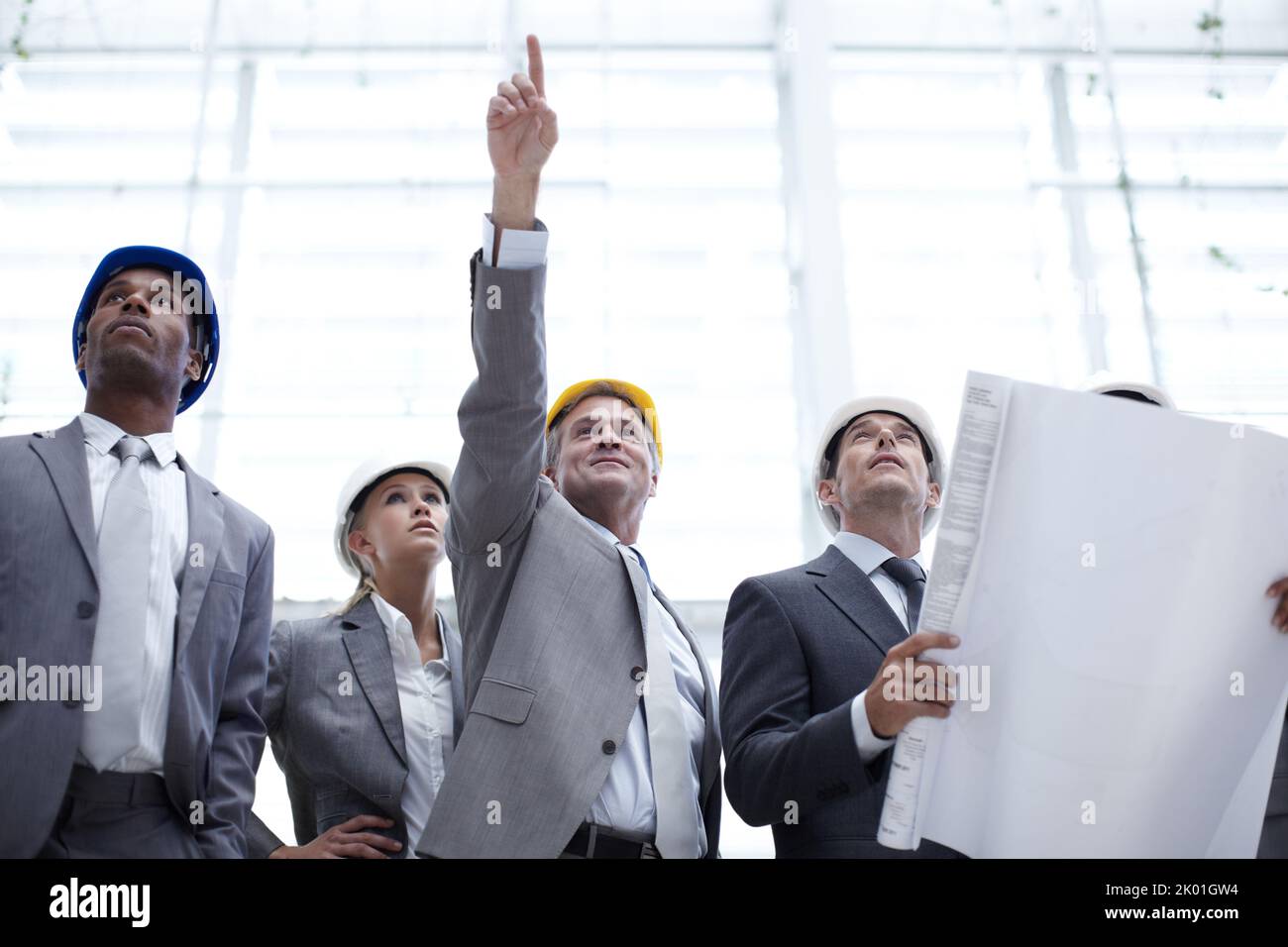 Unser Logo sollte dorthin gehen. Eine Aufnahme einer vielfältigen Gruppe von Technikern, die auf ein Gebäude zeigen, während sie Baupläne halten. Stockfoto
