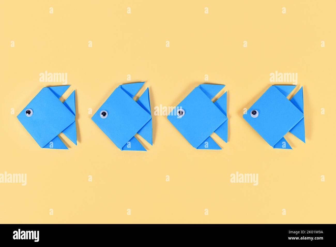 Blauer Origami-Papierfisch schwimmt in einer Reihe auf gelbem Hintergrund Stockfoto