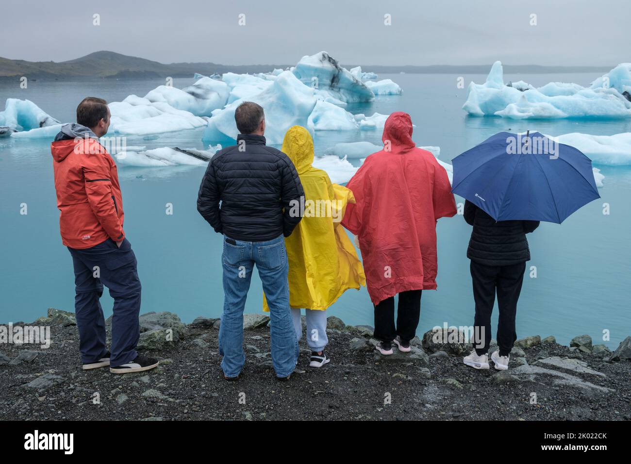 Touristen in farbenfrohen Wasserproofs, die die Eisberge in der Jokulsarlon Gletscherlagune, Island, betrachten Stockfoto