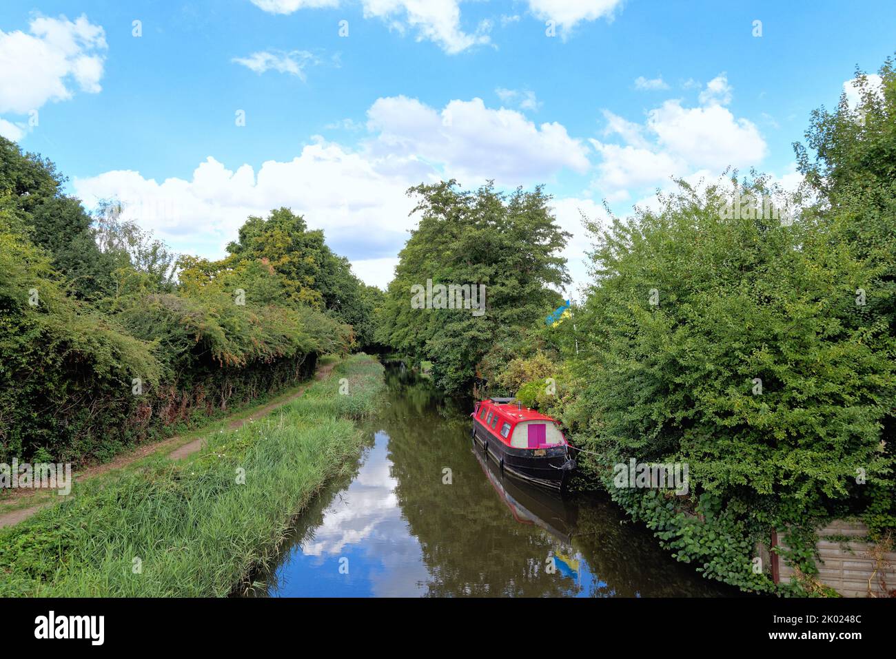 Ein Schmalboot mit einem roten Überbau, das auf dem Navigationskanal des Flusses Wey auf dem Land in der Nähe von Ripley Surrey, England, festgemacht ist Stockfoto