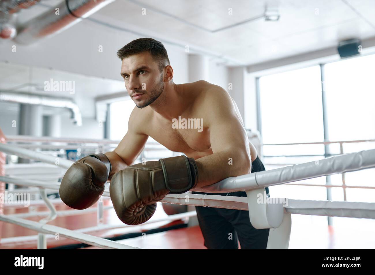 Der junge Boxer, der auf den Kampf wartet, lehnte sich an einem Ringseil Stockfoto