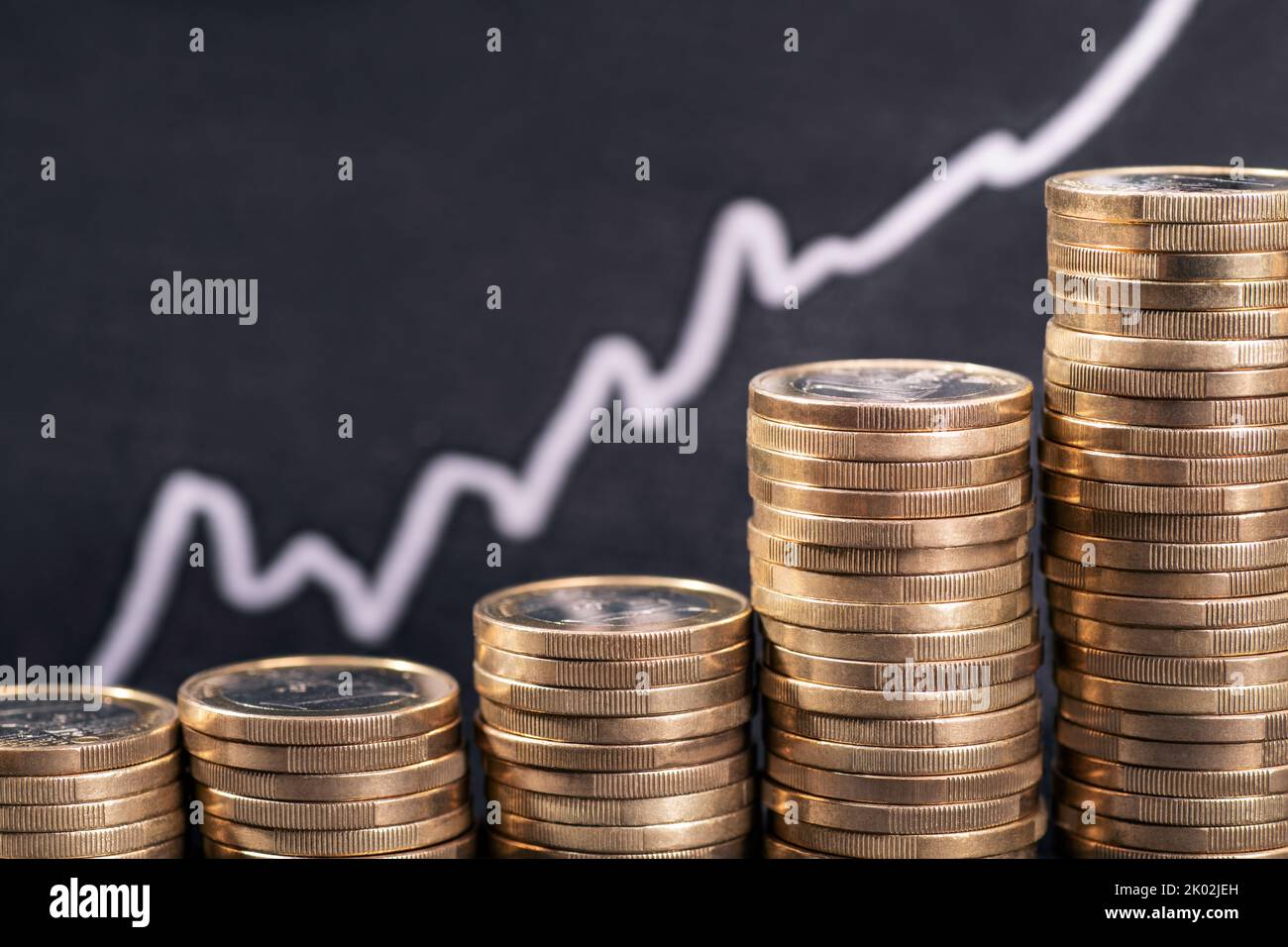 Steigende Preise und Kosten aufgrund der Inflation. Stapel von Münzen vor einer Grafik mit steigender Kurve. Stockfoto