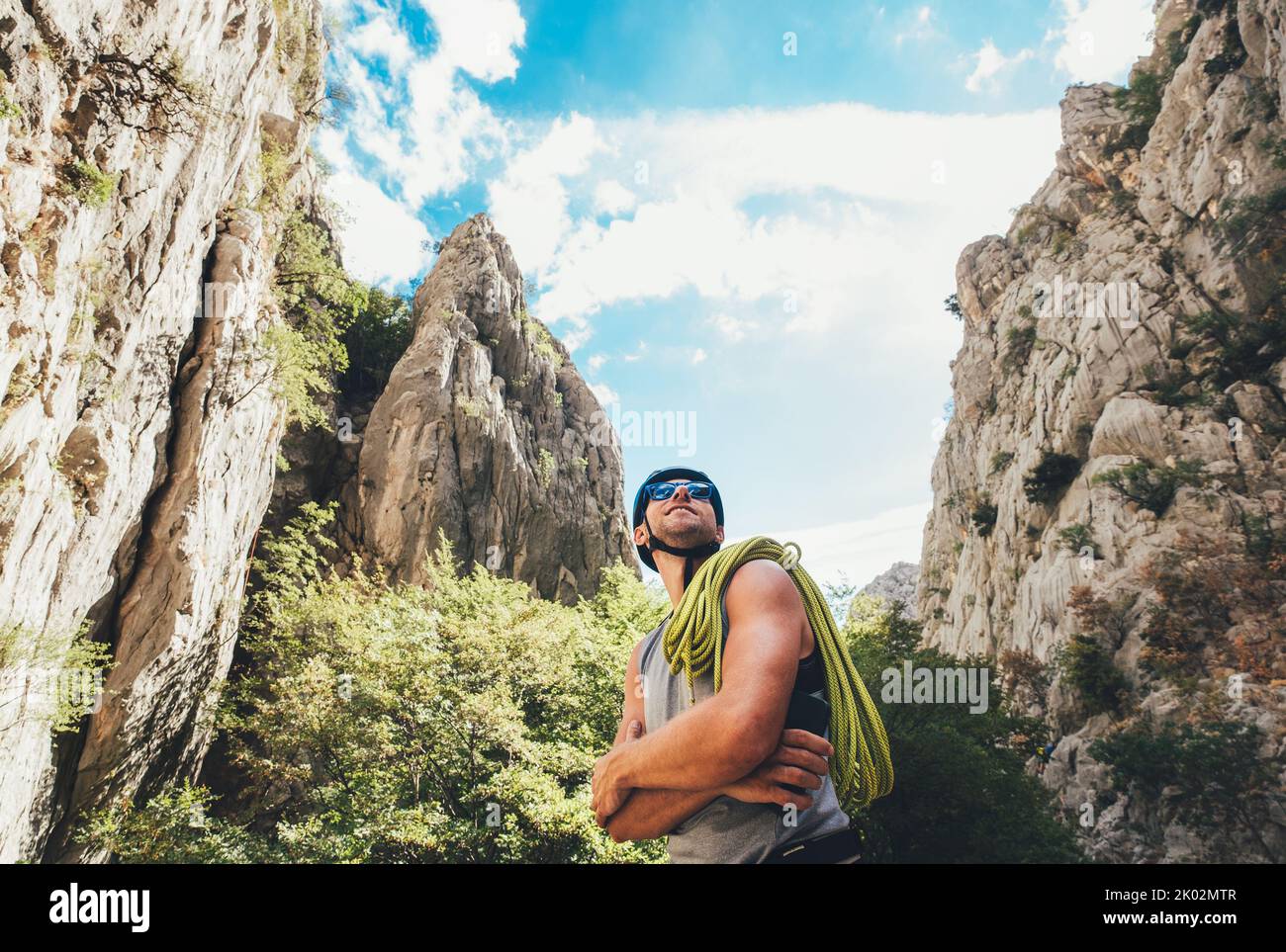 Lächelnder Bergsteiger Mann in Schutzhelm und Sonnenbrille mit Kletterseil auf der Schulter in der Paklenica zwischen Felswänden. Aktive extreme s Stockfoto