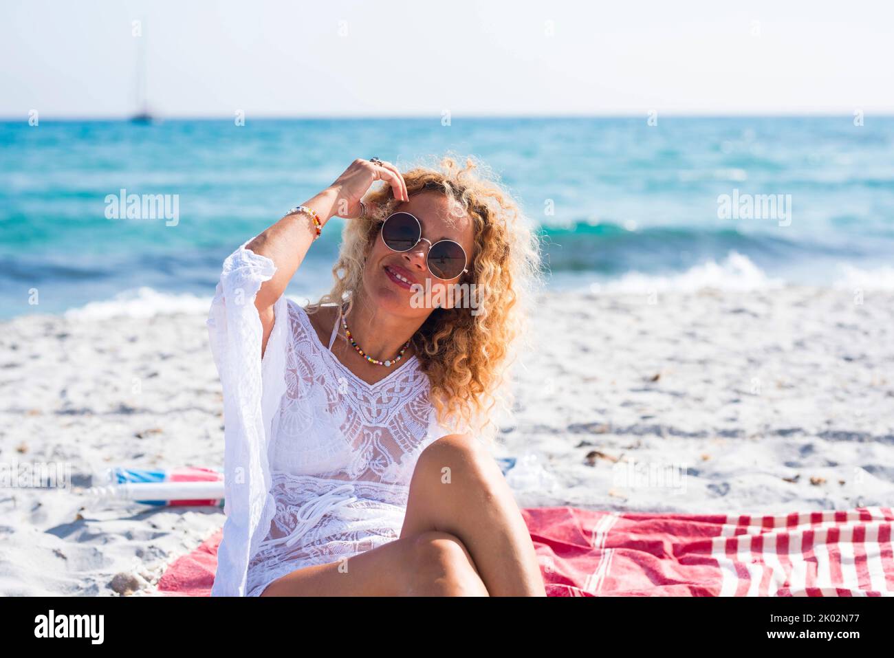 Porträt einer Frau mit einem Lächeln und einem Posen am Strand auf weißem Sand und blauem Ozean im Hintergrund. Happy Tourism Freizeitangebot Konzept. Weibliche Menschen im Sommerferienleben Stockfoto
