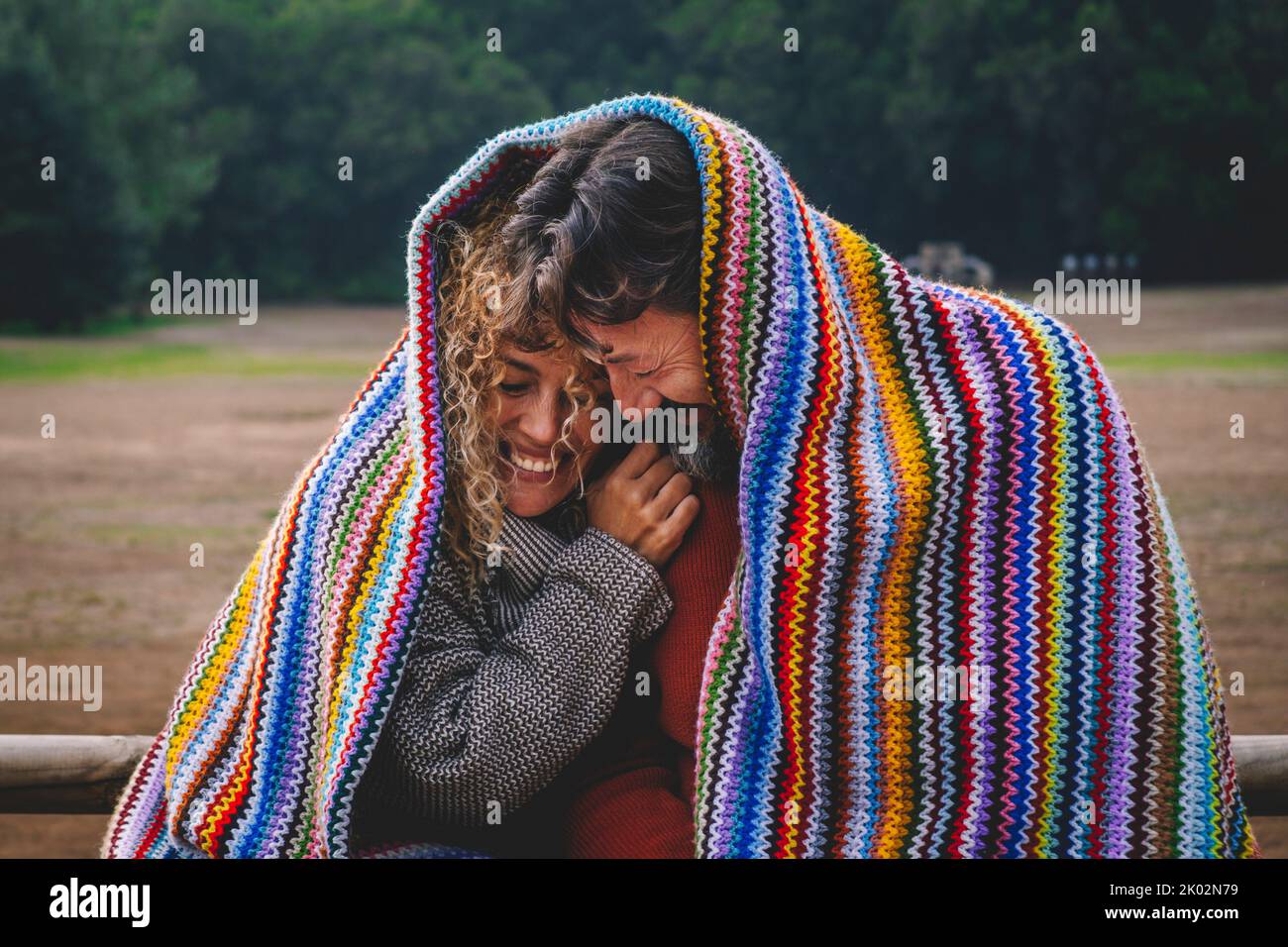 Intime lustige und glückliche Momente mit einem erwachsenen Paar bei Freizeitaktivitäten im Freien, die mit einer bunten Strickdecke im Park bedeckt sind. Mann und Frau verlieben sich im Park und sind miteinander verbunden Stockfoto
