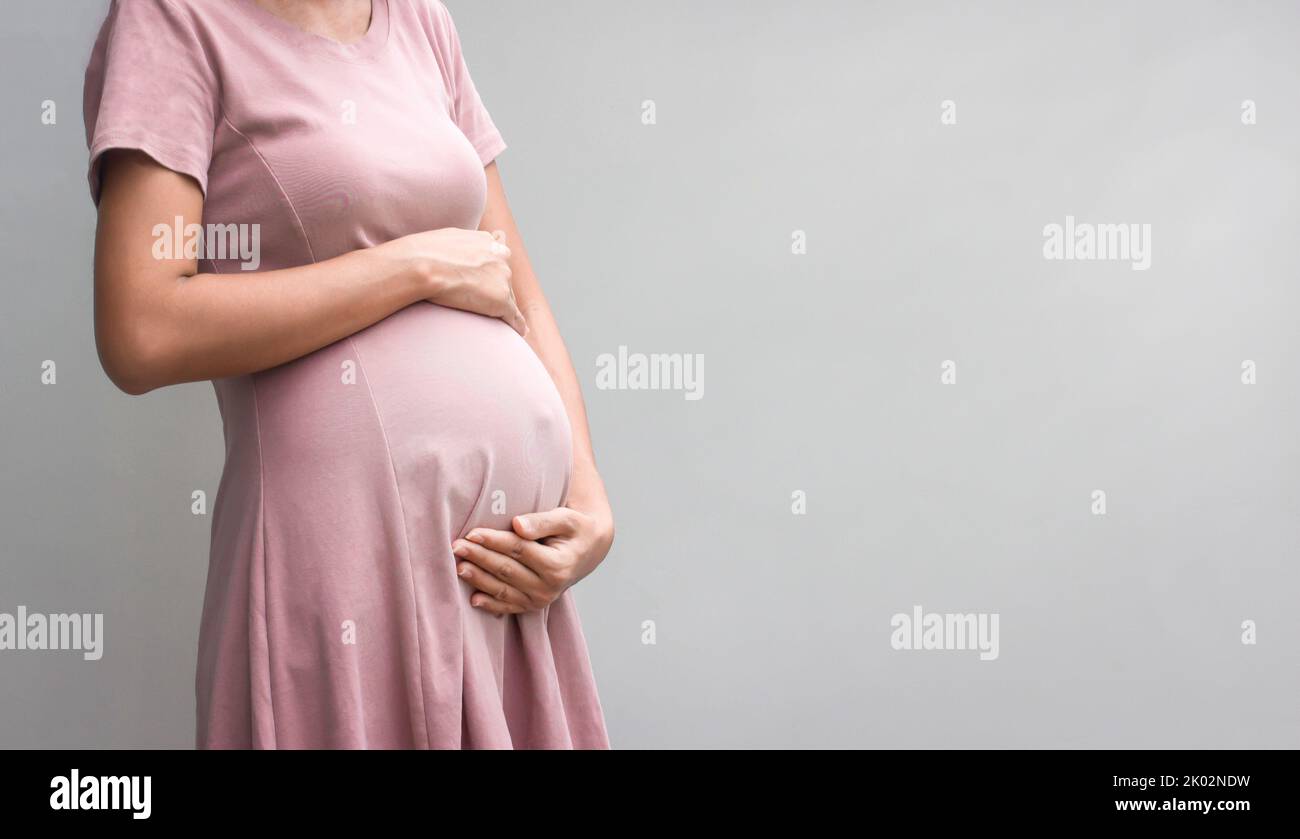 Schwangere im Kleid hält die Hände auf dem Bauch auf weißem Hintergrund. Konzept. Nahaufnahme, Kopierbereich. Stockfoto