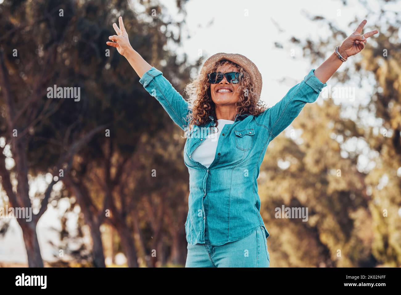 Überglücklich Menschen glückliche Frau hob ihre Arme mit Sieg Geste und lächeln mit grünen Bäumen Natur im Freien Hintergrund. Fröhliche weibliche Menschen in der Freizeit touristische Aktivität draußen. Lady hat Spaß Stockfoto