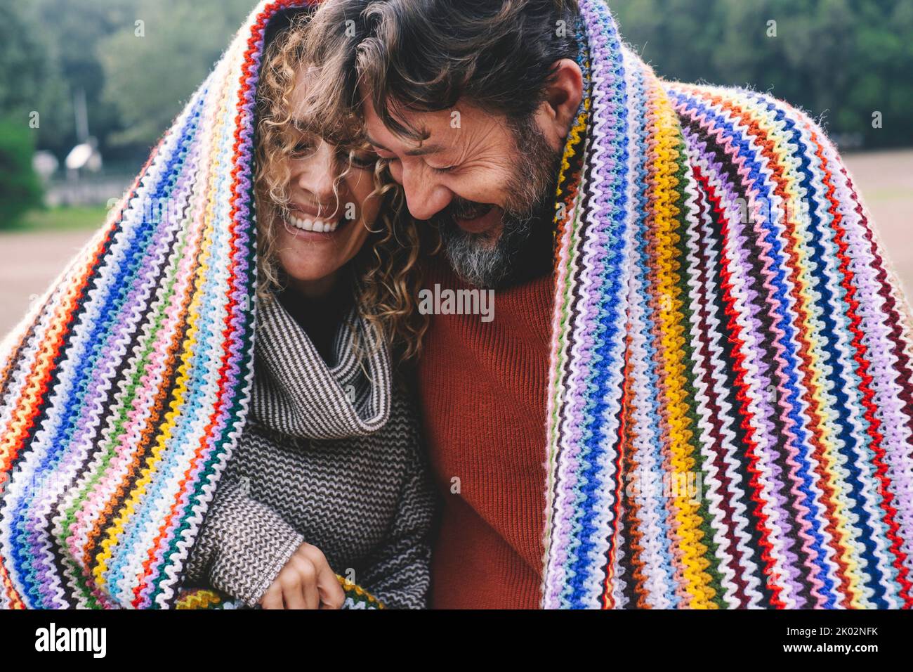 Überglücklich erwachsenes kaukasisches Paar unter einem bunten Cover lacht und hat Spaß zusammen mit Liebe und Freundschaft. Junge ältere Menschen in Outdoor-Freizeit romantische Aktivität. Mann und Frau lachen viel Stockfoto
