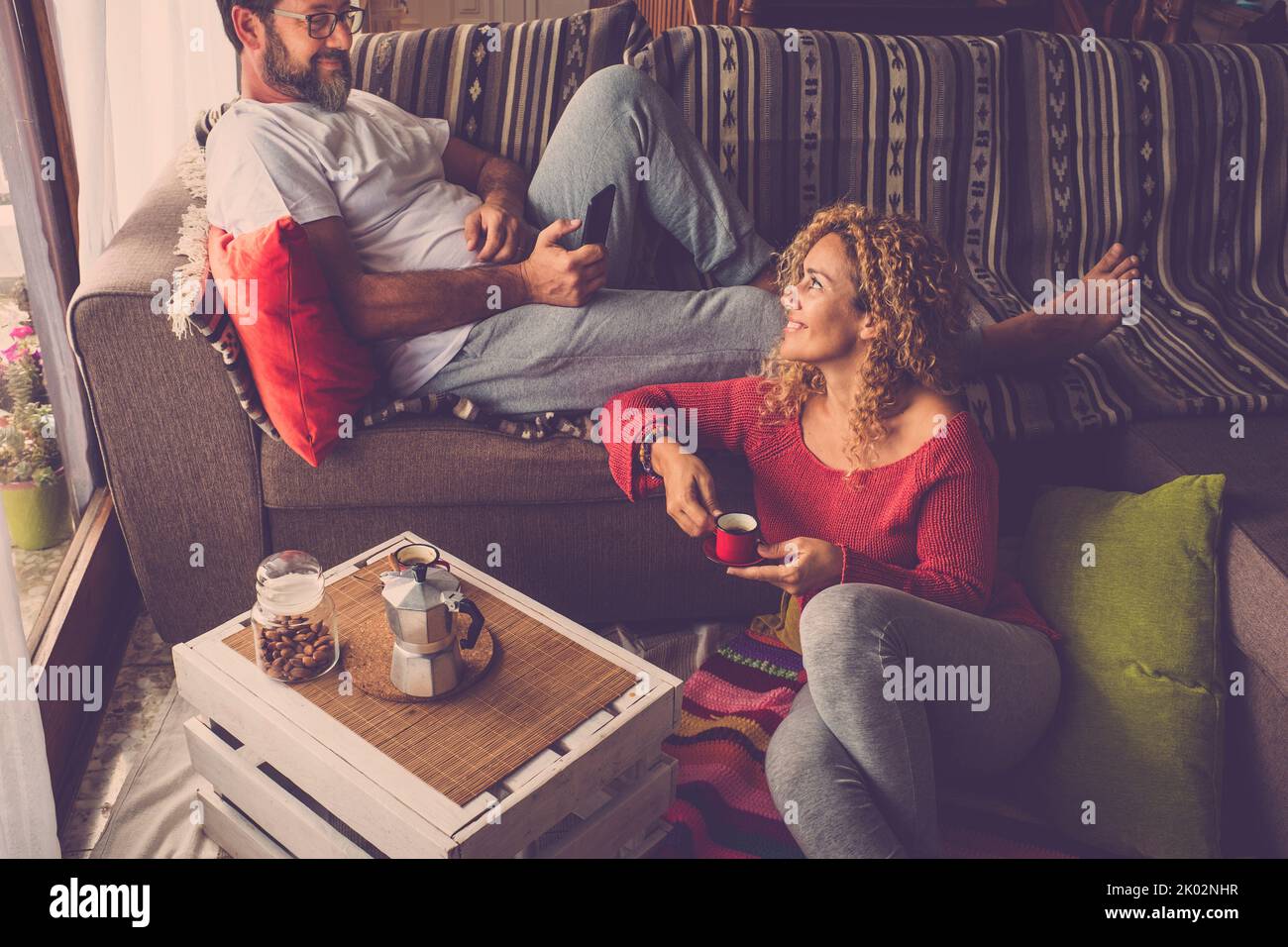 Paar in romantischer Freizeit zu Hause beim Frühstück zusammen. Mann telefoniert und Frau trinkt Kaffee lächelnd. Das wirkliche Leben und die Menschen genießen Wohnung. Sonntagszeit und Feiertag Stockfoto