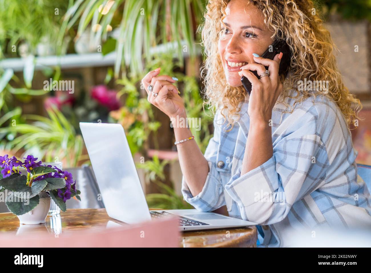 Erwachsene Frau, die am Telefon anruft und auf dem Tisch sitzt. Ziemlich weibliche Leute, die am Schreibtisch sprachen und mobile Handys und Laptops benutzten. Geschäftsfrau verwaltet Online-E-Commerce-Shop für geschäftliche Aktivitäten Stockfoto