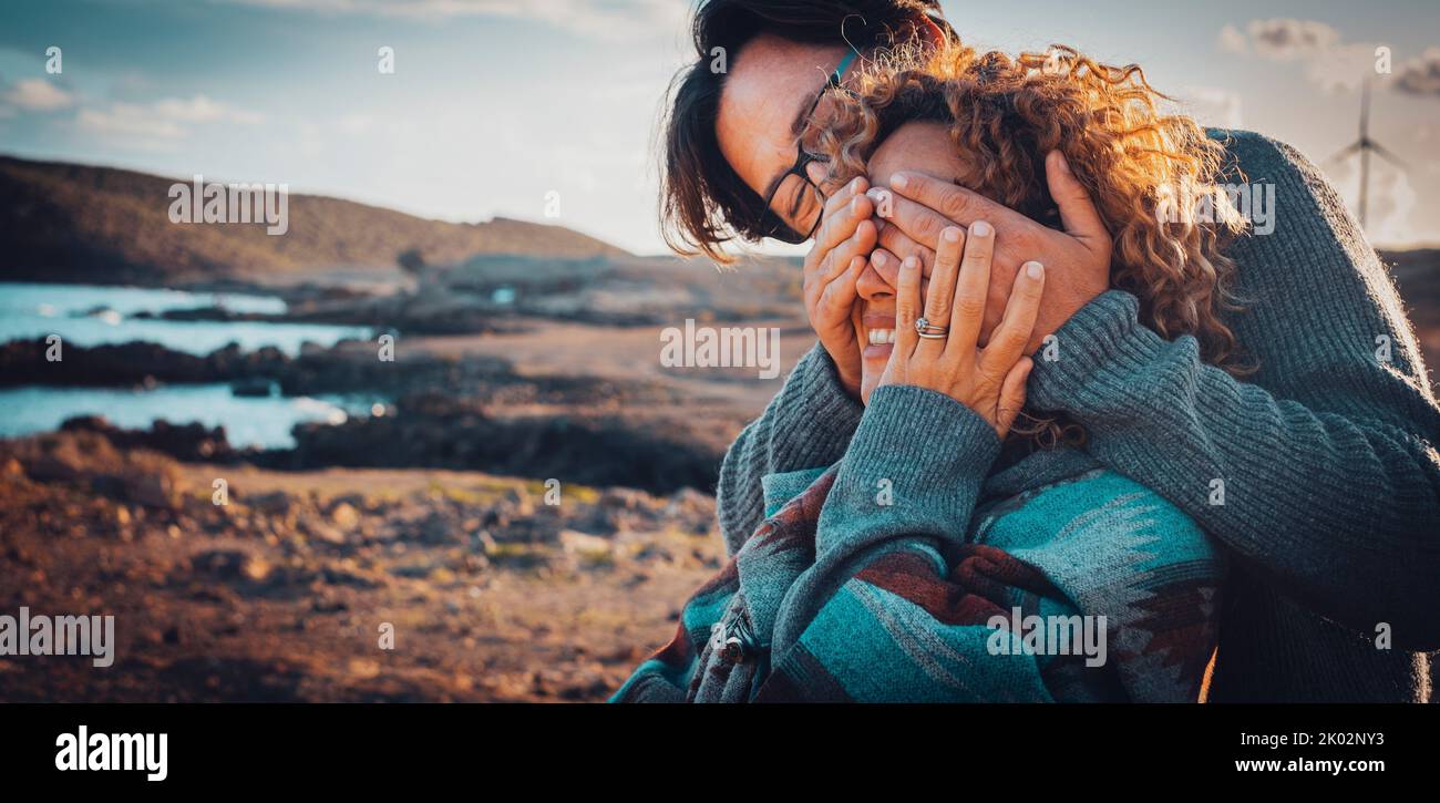 Genossen erwachsenen Paar im Freien Freizeitaktivitäten mit Mann legte seine Hände, um Frau Augen zu decken. Meeresstrand und blauer Himmel im Hintergrund. Reisen und Fernweh Lifestyle Menschen Konzept Stockfoto