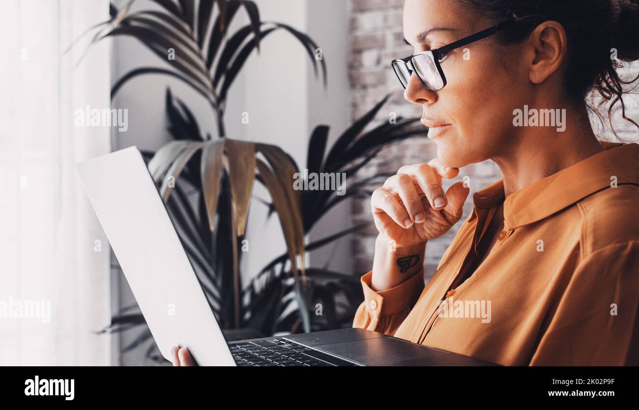 Seitenansicht weiblicher Menschen beim Lesen und Verwenden eines Laptops konzentriert. Intelligentes Arbeiten zu Hause. Erwachsene Frau mit Brille, die online arbeitet. Moderne Lifestyle-Menschen mit Online-Verbindung Lebensstil Stockfoto