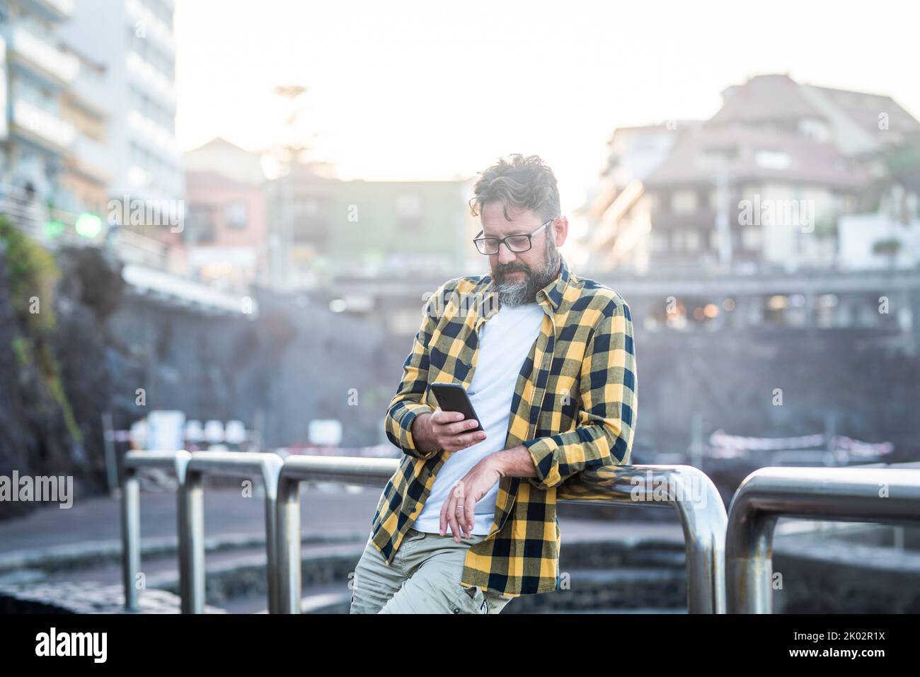 Junge Erwachsene reifen kaukasischen Mann mit Handy im Freien mit Wireless Internet kostenlose Verbindung. Männliche Menschen nutzen an sonnigen Tagen in der Stadt ein Mobilfunkgerät. Stadtgebäude im Hintergrund Stockfoto