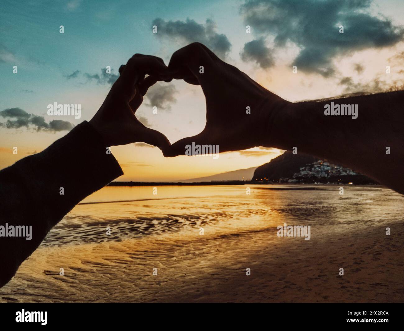 Pov des Paares tun Herz Geste Symbol mit Händen zusammen am Strand in Sommerurlaub Urlaub mit erstaunlichen Himmel und bunten Sonnenuntergang im Hintergrund. Menschen und Beziehungen Stockfoto