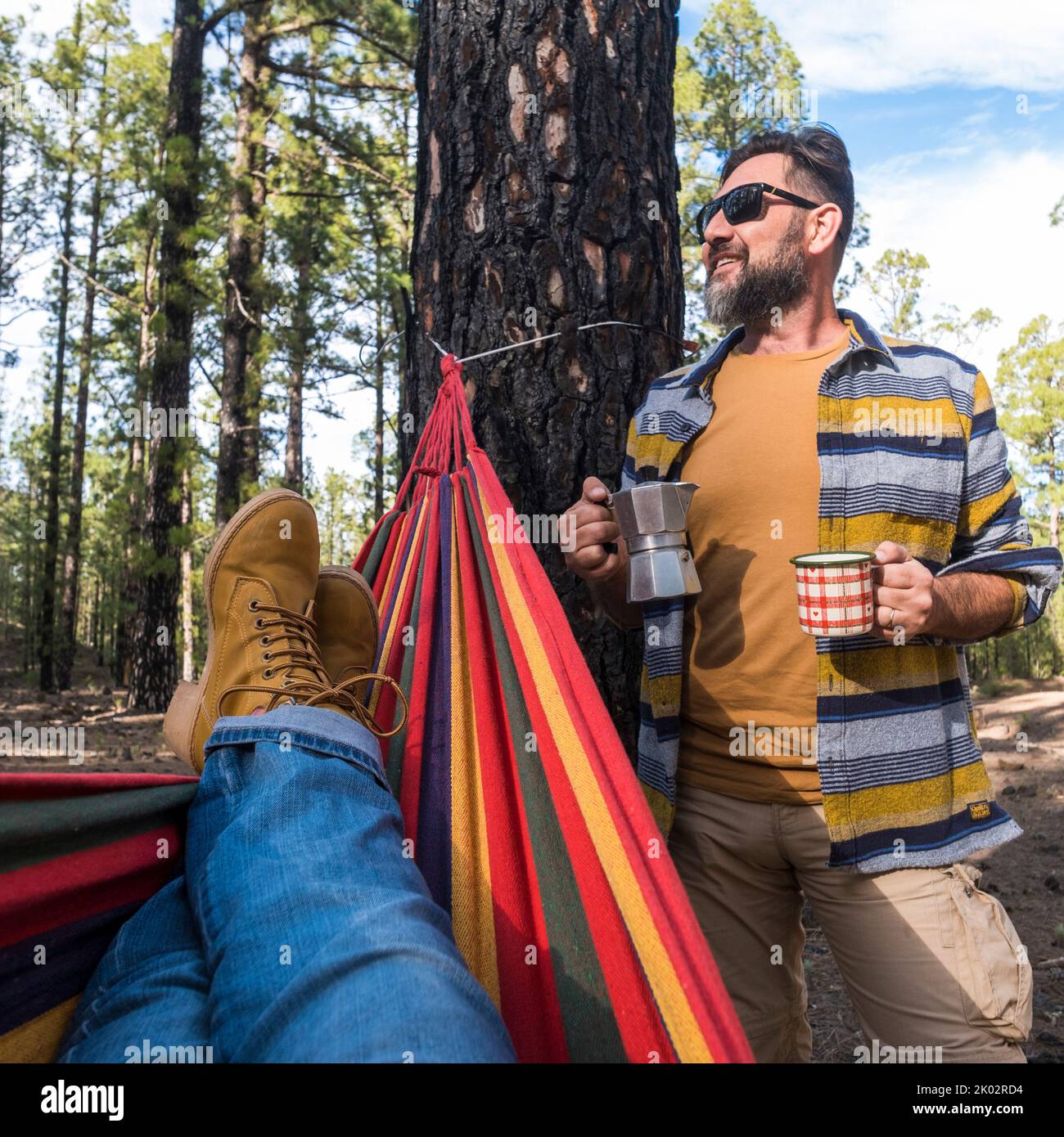 Glücklicher Erwachsener kaukasischen Paar genießen Sie die Natur Outdoor-Freizeit Camping-Aktivität - Frau Beine pov auf Hängematte und Mann mit Kaffee stehen - Umwelt und Natur Urlaub Stockfoto Glücklicher Erwachsener kaukasischen Paar genießen Sie die Natur Outdoor-Freizeit Camping-Aktivität - Frau Beine pov auf Hängematte und Mann mit Kaffee stehen - Umwelt und Natur Urlaub Stockfoto