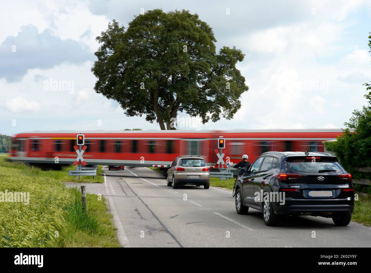 Deutschland, Bayern, Landkreis Altötting, Landstraße, Bahnübergang mit Schranken, Nahverkehrszug durchfahren, Waggons warten Stockfoto