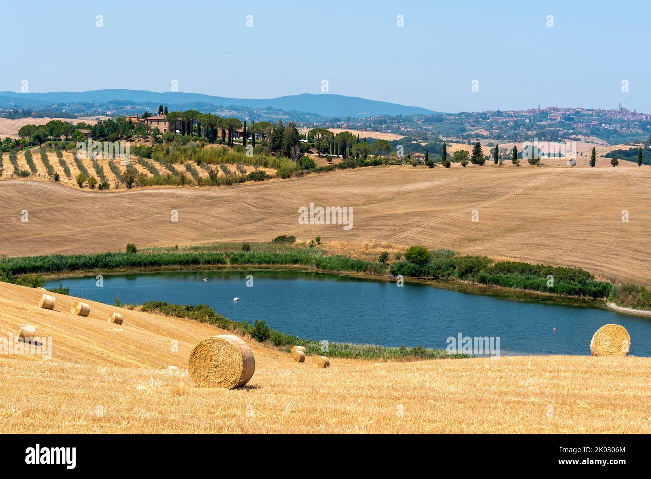 Geerntete Getreidefelder, Teich, Anwesen mit Zypressen, am Horizont die Stadt Siena, Toskana, Italien Stockfoto