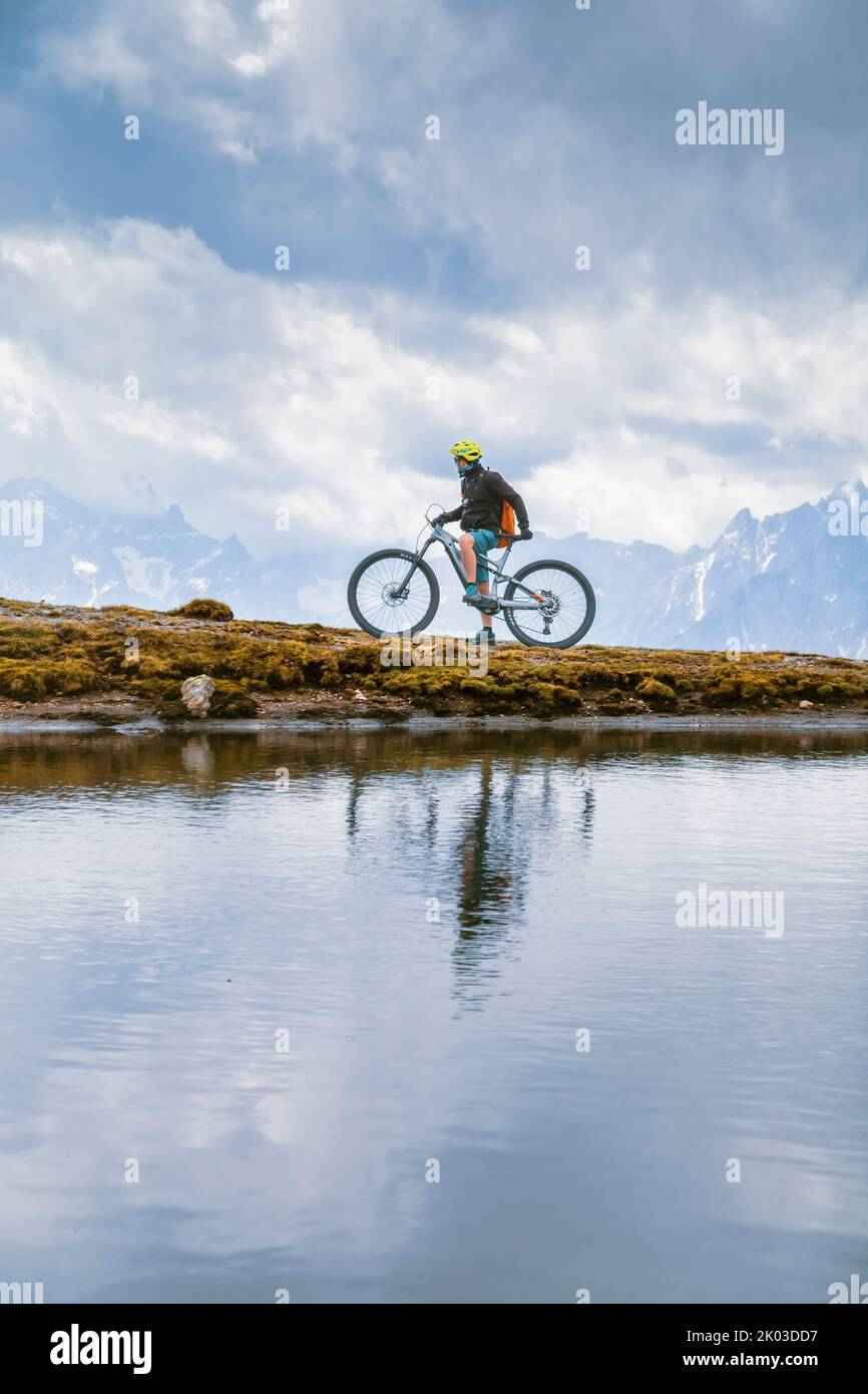 Italien, Südtirol, Bozen, Innichen. Fahrer mit E-Bike, Reflexion in einem alpinen kleinen See an einem bewölkten Tag Stockfoto
