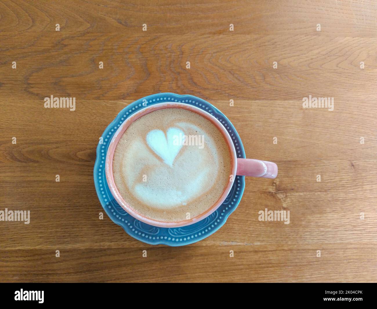 Rote Tasse Kaffee auf der blauen Untertasse mit herzförmiger Milchkunst auf dem Holztisch Stockfoto