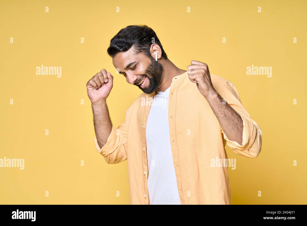 Glücklicher indischer Mann, der in Ohrhörern tanzt und Musik auf Gelb hört. Stockfoto