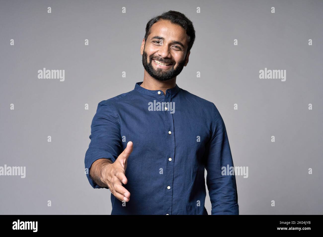Lächelnder indischer Geschäftsmann streckte die Hand für einen Handschlag isoliert auf grau aus. Stockfoto