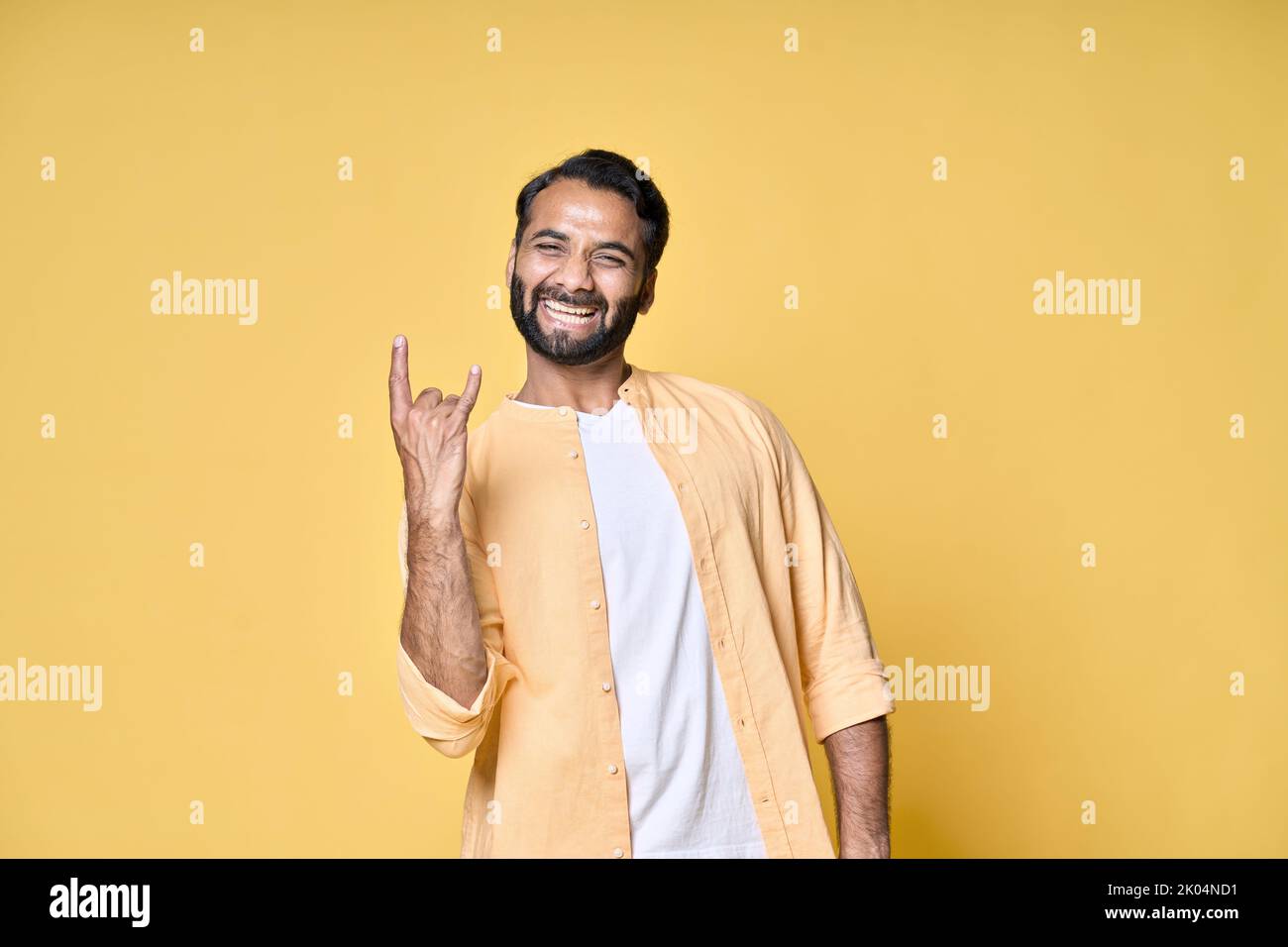 Glücklicher indischer Mann zeigt Rock n Roll Hörner Handgeste isoliert auf gelb. Stockfoto
