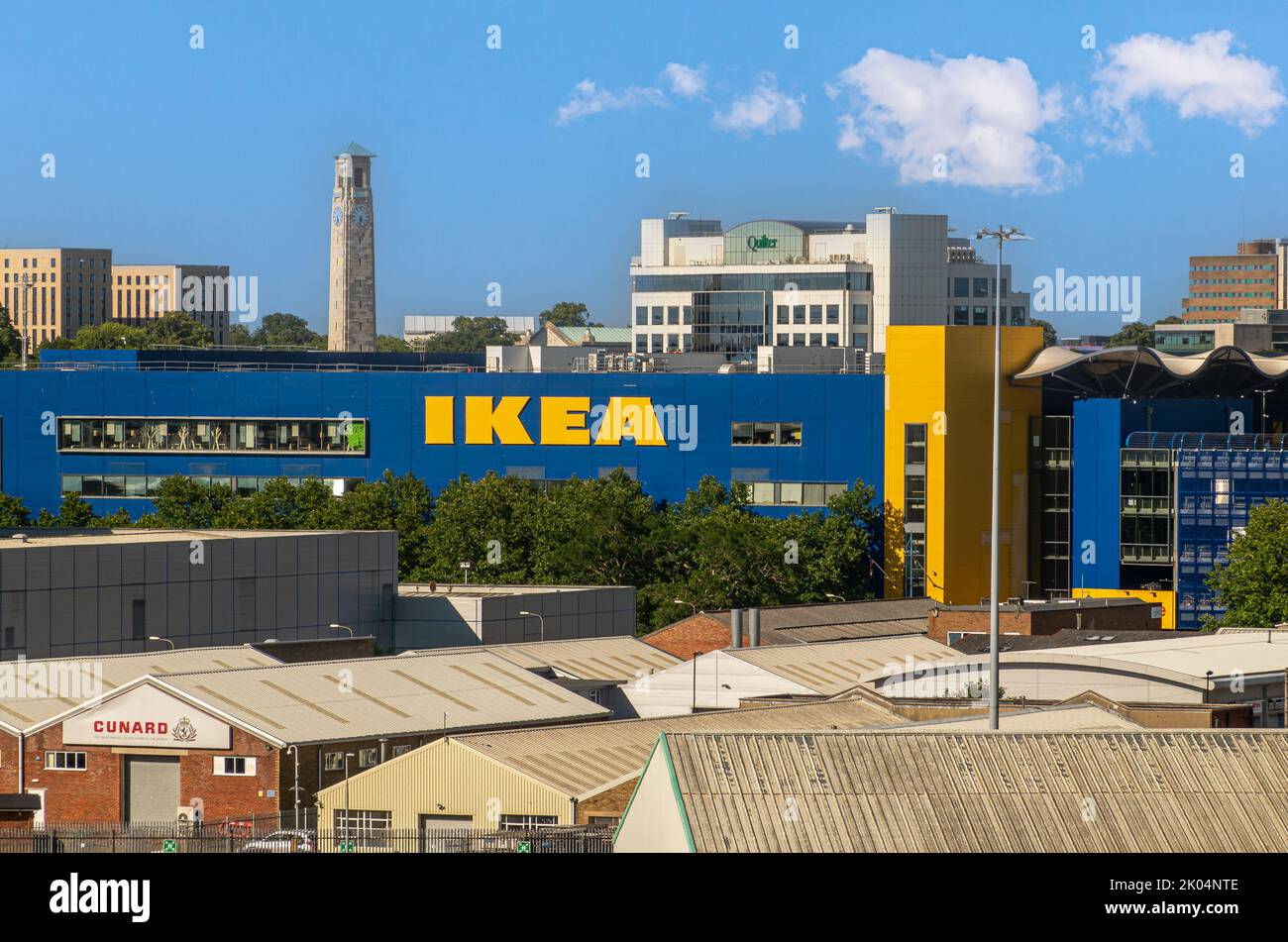 Southampton, England, Großbritannien - 7. Juli 2022: Hafenlandschaft. Der beigefarbene, hohe Uhrenturm des SeaCity Museums überguckst das blau-gelbe IKEA-Gebäude im Stadtbild un Stockfoto