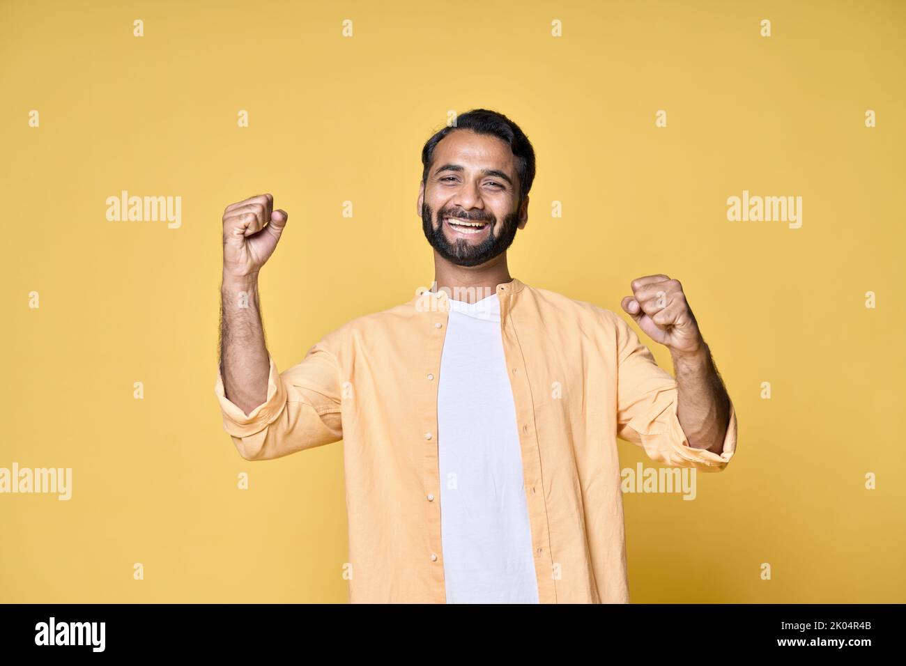 Fröhlicher, fröhlicher indischer Mann, der auf gelbem Hintergrund die Fäuste hebt. Stockfoto