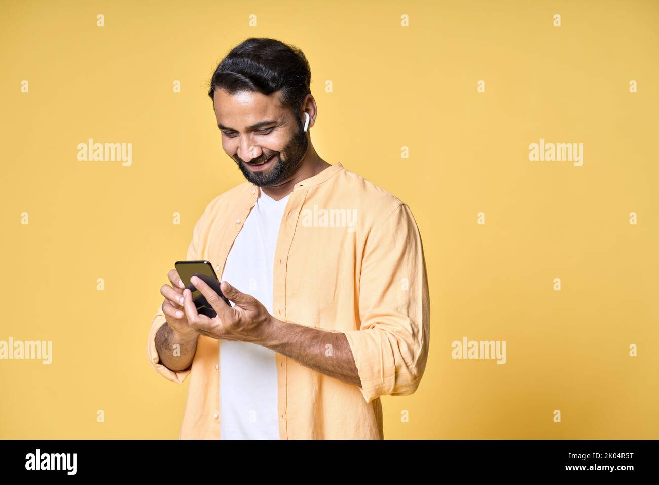 Indischer Mann trägt Ohrstöpsel mit Mobiltelefon isoliert gelben Hintergrund. Stockfoto