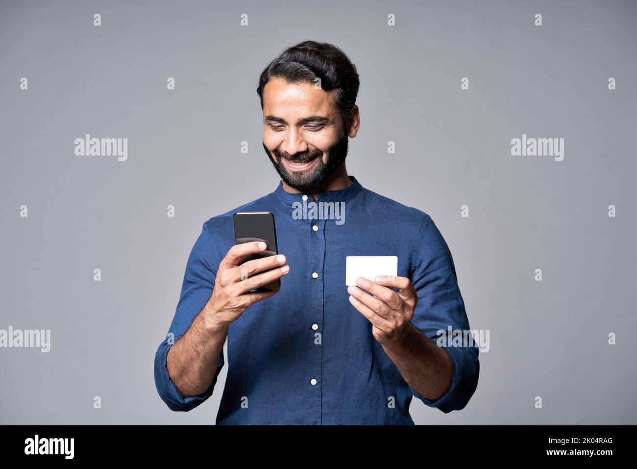 Glücklicher indischer Geschäftsmann, der Telefon und Kreditkarte mit der mobilen Bank-App hält. Stockfoto