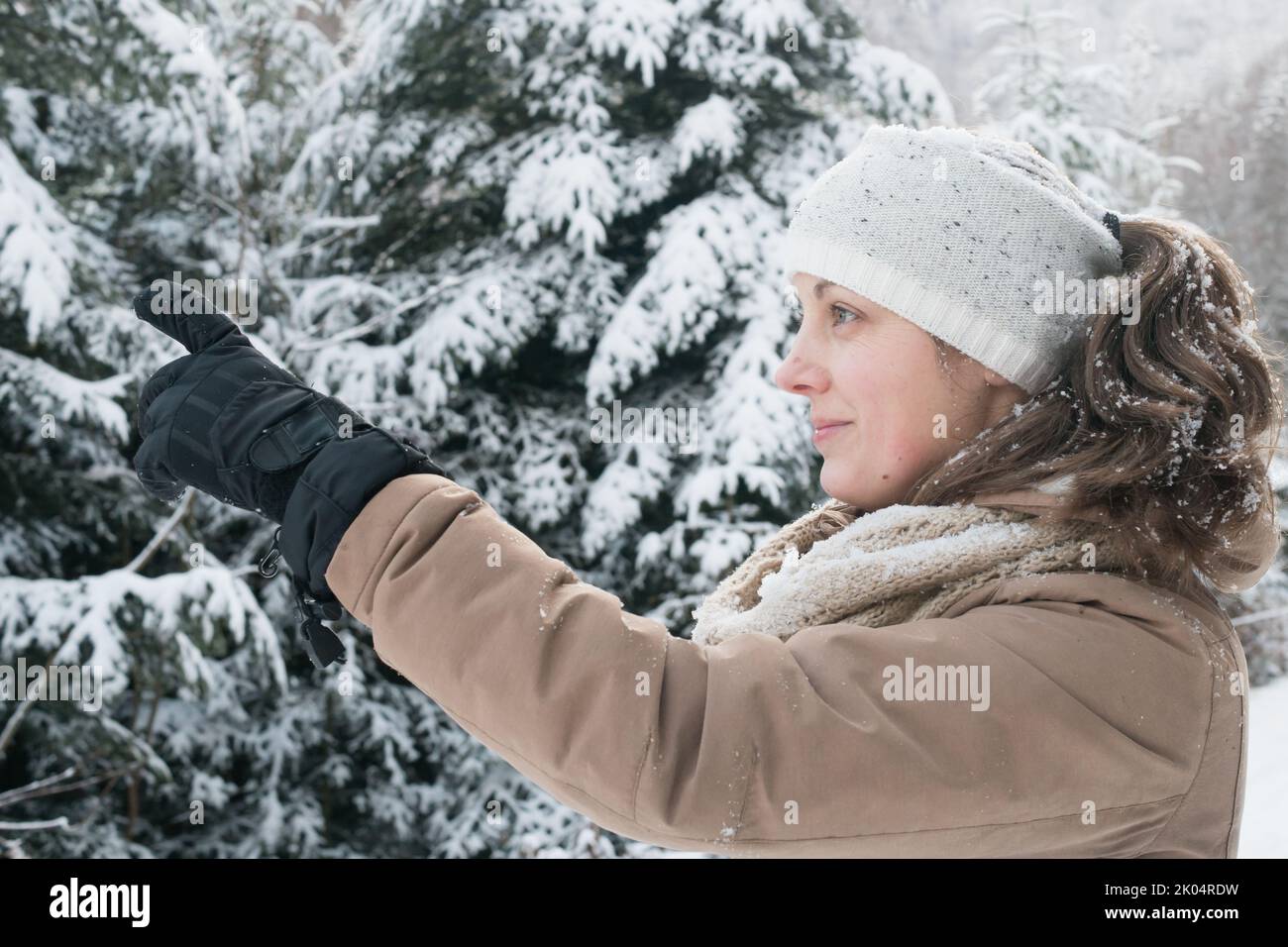 Lächelnde kaukasische Frau mittleren Alters, die mit ihrem Finger eine wunderschöne Winterlandschaft zeigt. Sie trägt Stirnband, Schal und Handschuhe. Keine Make-up-Frau. Keine Retuschentuschentdürfen Stockfoto