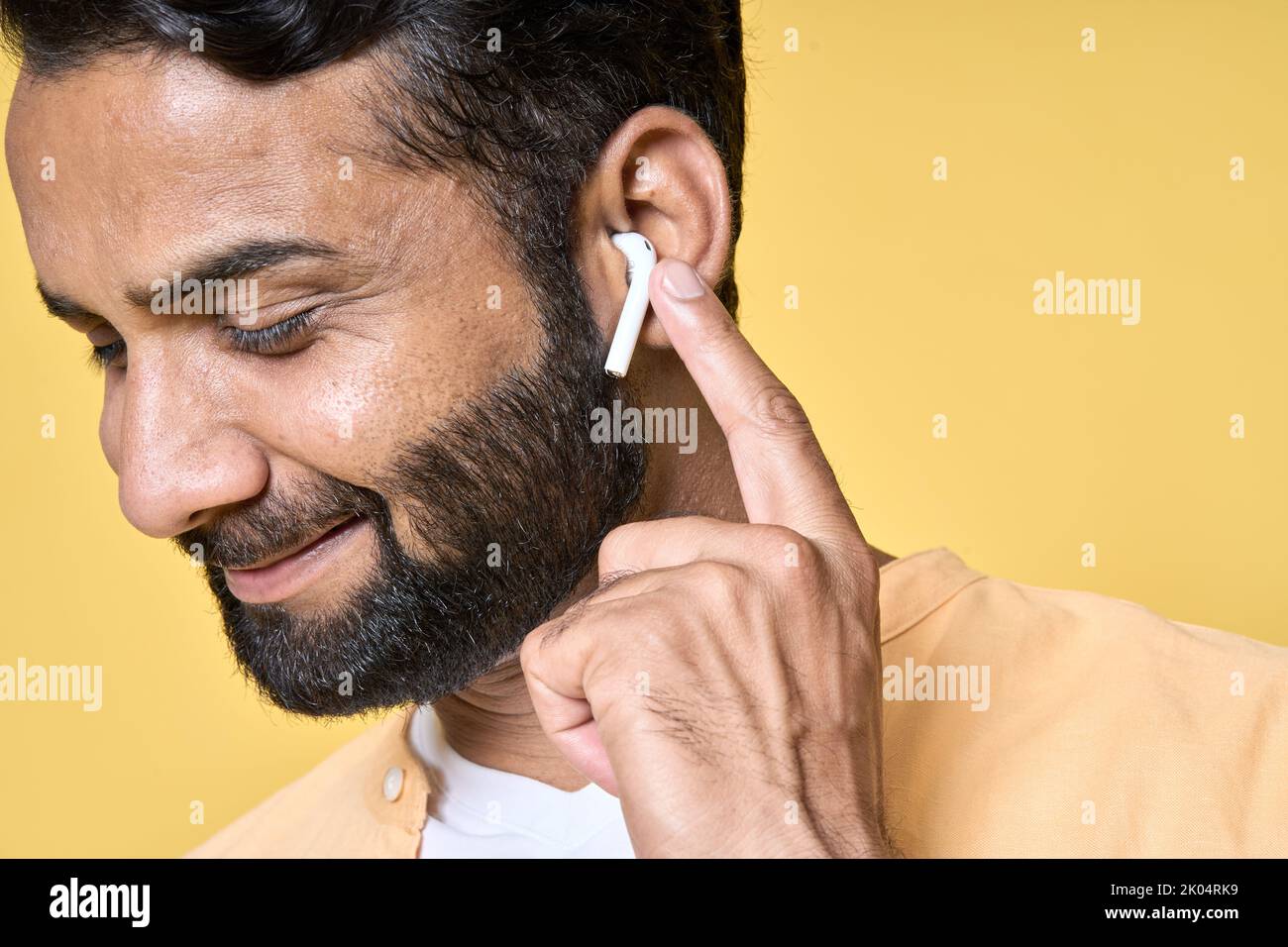 Glücklicher bärtiger indischer Mann, der Ohrstöpsel trägt und Musik oder Podcast hört. Nahaufnahme Stockfoto
