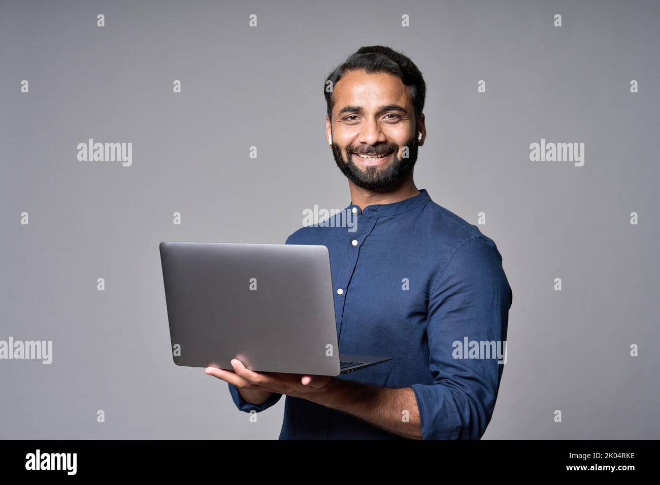 Glücklicher indischer Geschäftsmann hält Laptop isoliert auf grauem Hintergrund. Stockfoto