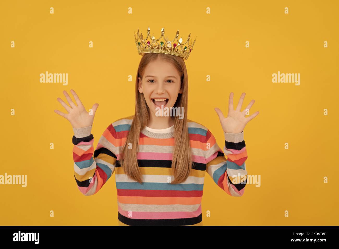 Frohes Teenager-Kind in Königskrone auf gelbem Hintergrund Stockfoto